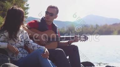 一对年轻夫妇在海边玩吉他唱歌，在山河旁边的夏天。 3840x2160